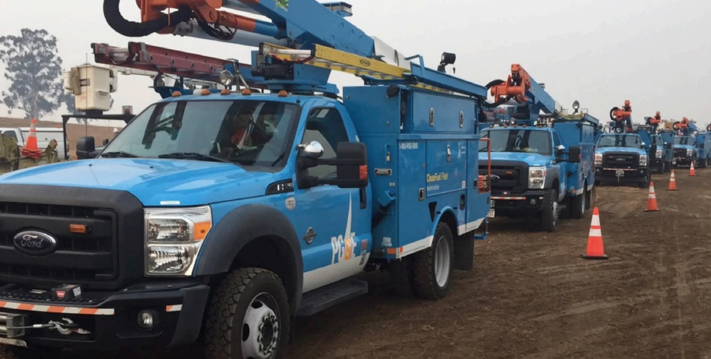 A line of PG&E utility bucket trucks staged in the field